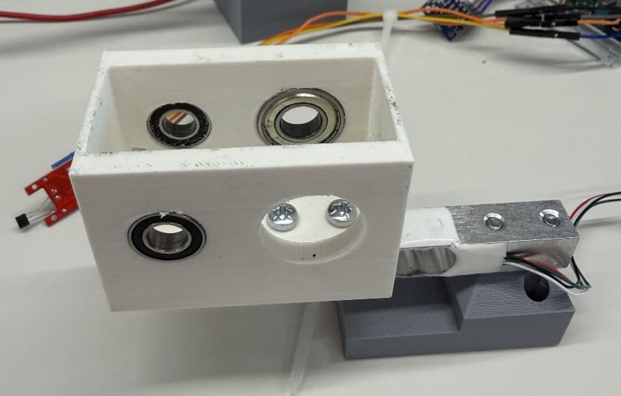 The printed gearbox housing with two bearings, mounted on the load cell on a grey base, on a lab bench with wiring.